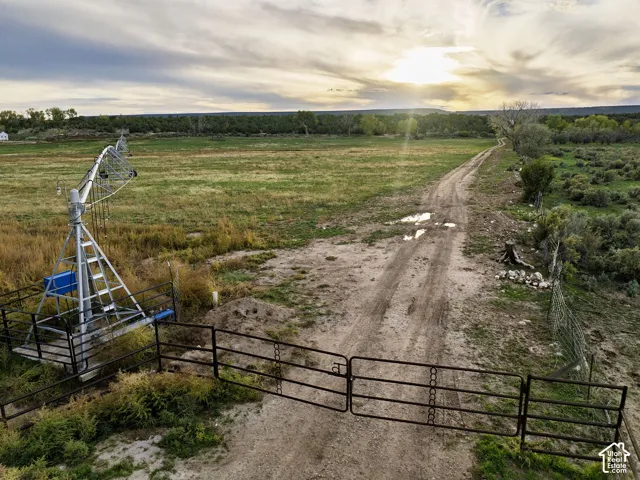 Expansive land featuring a metal gate, dirt track, agricultural irrigation system, and natural vegetation
