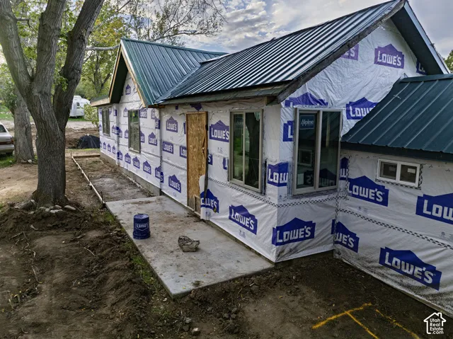Standing seam metal roof, multiple windows, concrete patio, concrete walkway, and established trees
