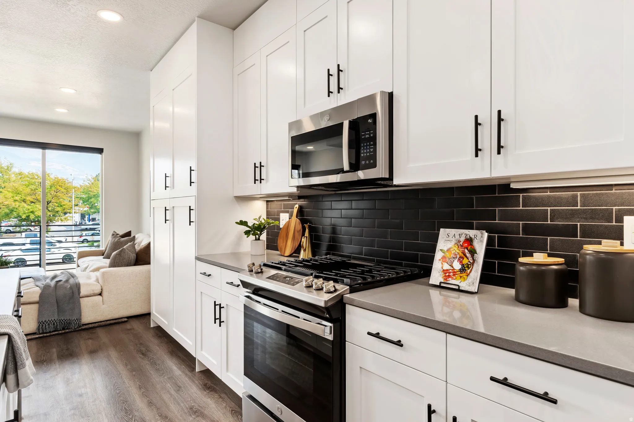 Kitchen featuring stainless steel appliances, white cabinetry, dark wood-style floors, recessed lighting, and light stone counters. Model Home