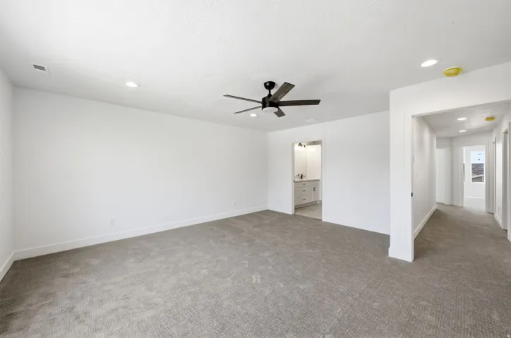 Spacious carpeted room featuring a ceiling fan, recessed lighting, and a white vanity with a rectangular sink and wall-mounted faucet in the adjacent space