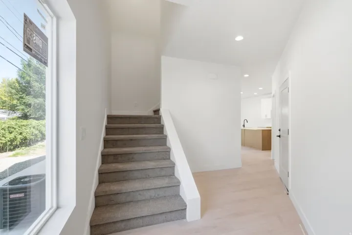 Bright entryway featuring light wood-finish flooring, a carpeted staircase, recessed lighting, and a window with white trim