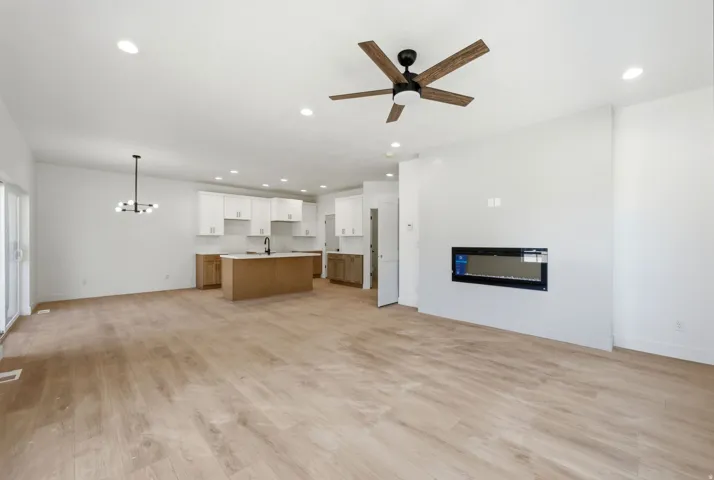Open-concept living space featuring wood-finish flooring, a contemporary linear fireplace, and a ceiling fan