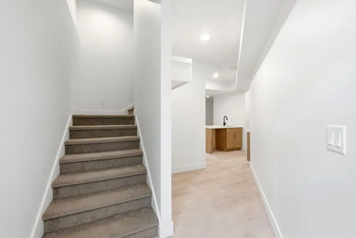 Carpeted staircase with white risers, contemporary recessed lighting, and light wood-finish flooring