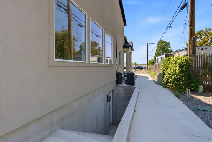 Stucco exterior with multiple windows, concrete walkway, and a concrete stairwell leading to a lower-level entry
