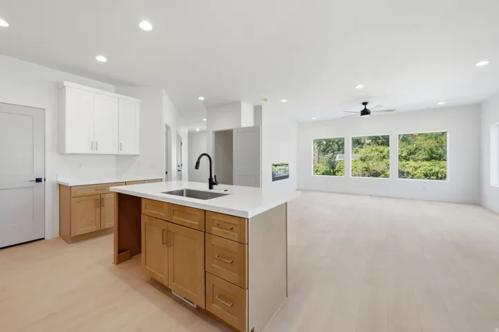 Open-concept living space featuring wood-finish flooring, recessed lighting, and a kitchen island with an undermount sink and matte black faucet