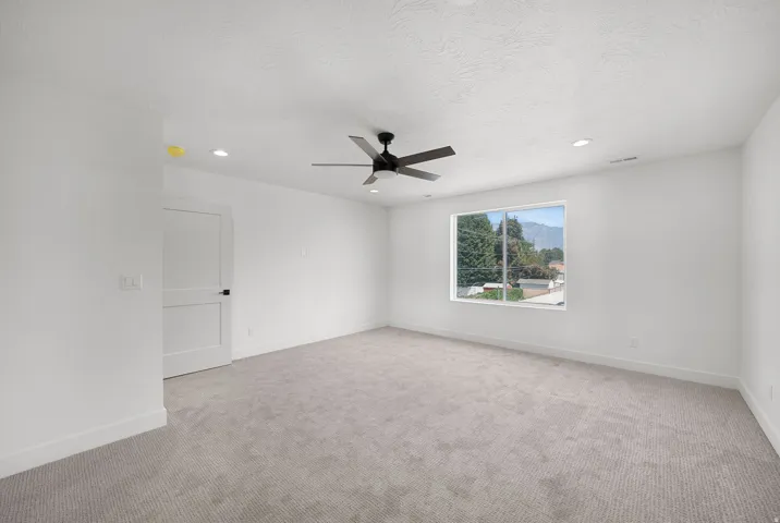 Spacious room featuring neutral carpeting, a large window, recessed lighting, and a ceiling fan