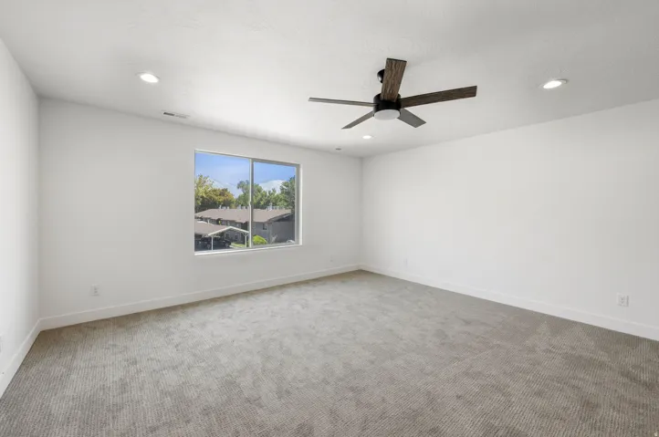 Recessed lighting, ceiling fan with wood-finish blades, large window, and light grey patterned carpet