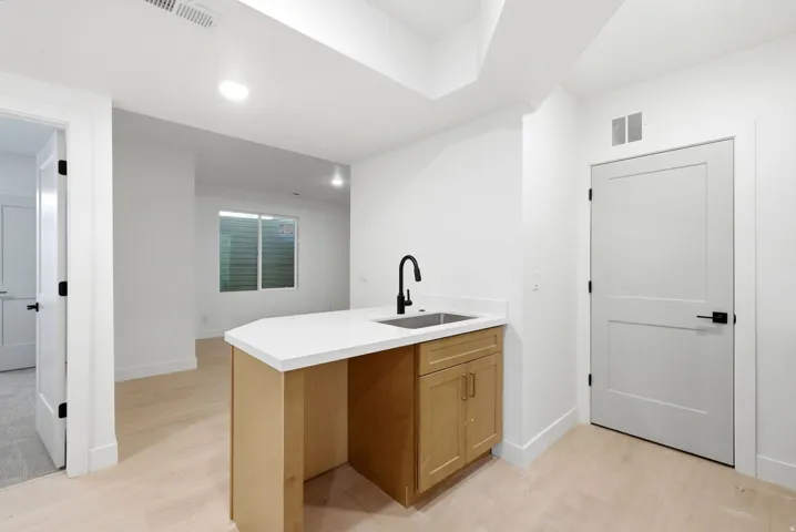 Kitchenette featuring light wood-finish cabinetry, a white countertop, a stainless steel sink, and a matte black faucet