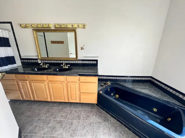 Bathroom with a jetted tub, double vanity, curtained shower, and tile patterned flooring