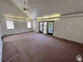 Empty room featuring high vaulted ceiling, dark carpet, and a ceiling fan