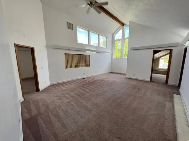 Unfurnished living room featuring high vaulted ceiling, beam ceiling, carpet floors, ceiling fan, and a textured ceiling