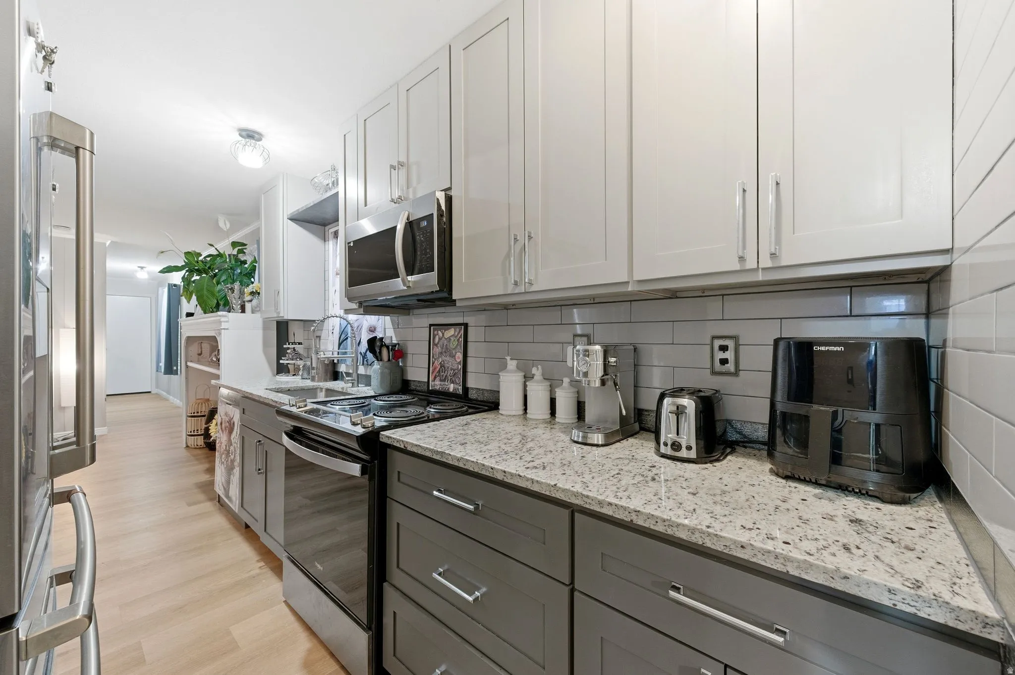 Kitchen with appliances with stainless steel finishes, light stone counters, white cabinetry, backsplash, and light wood-type flooring