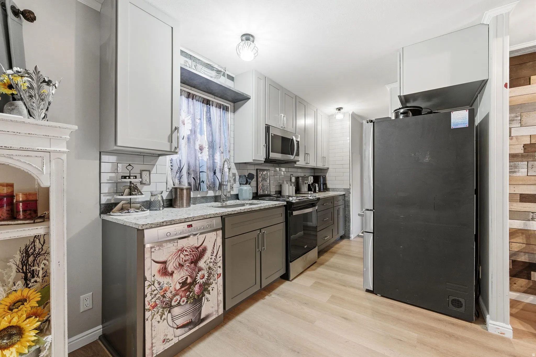 Kitchen with stainless steel appliances, light stone counters, gray cabinets, light wood-style flooring, and white cabinets