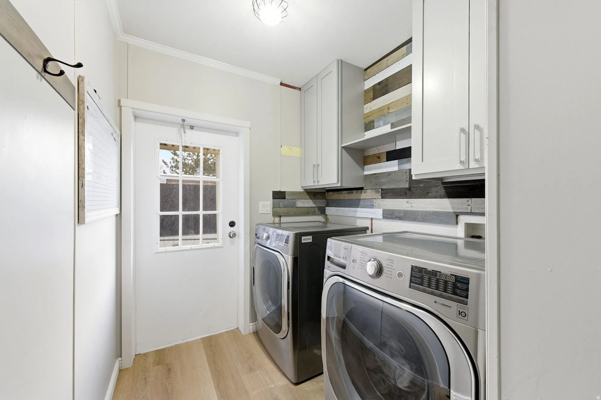 Laundry room featuring light wood-style flooring, crown molding, cabinet space, and washer and clothes dryer