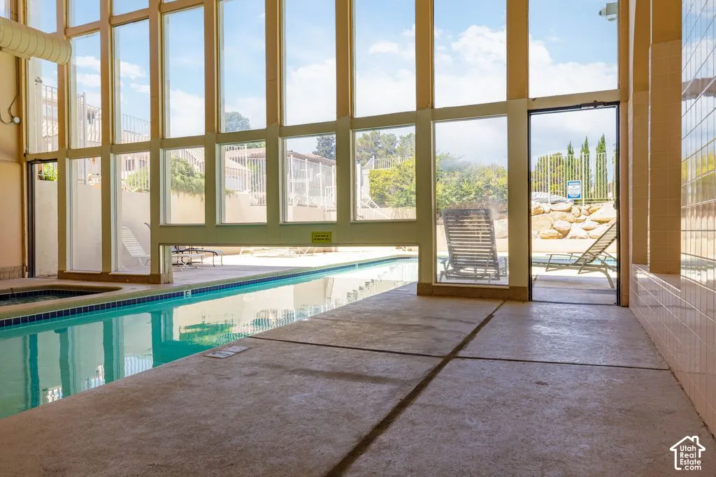 Indoor swimming pool area with expansive windows, an integrated spa, and direct access to an outdoor patio