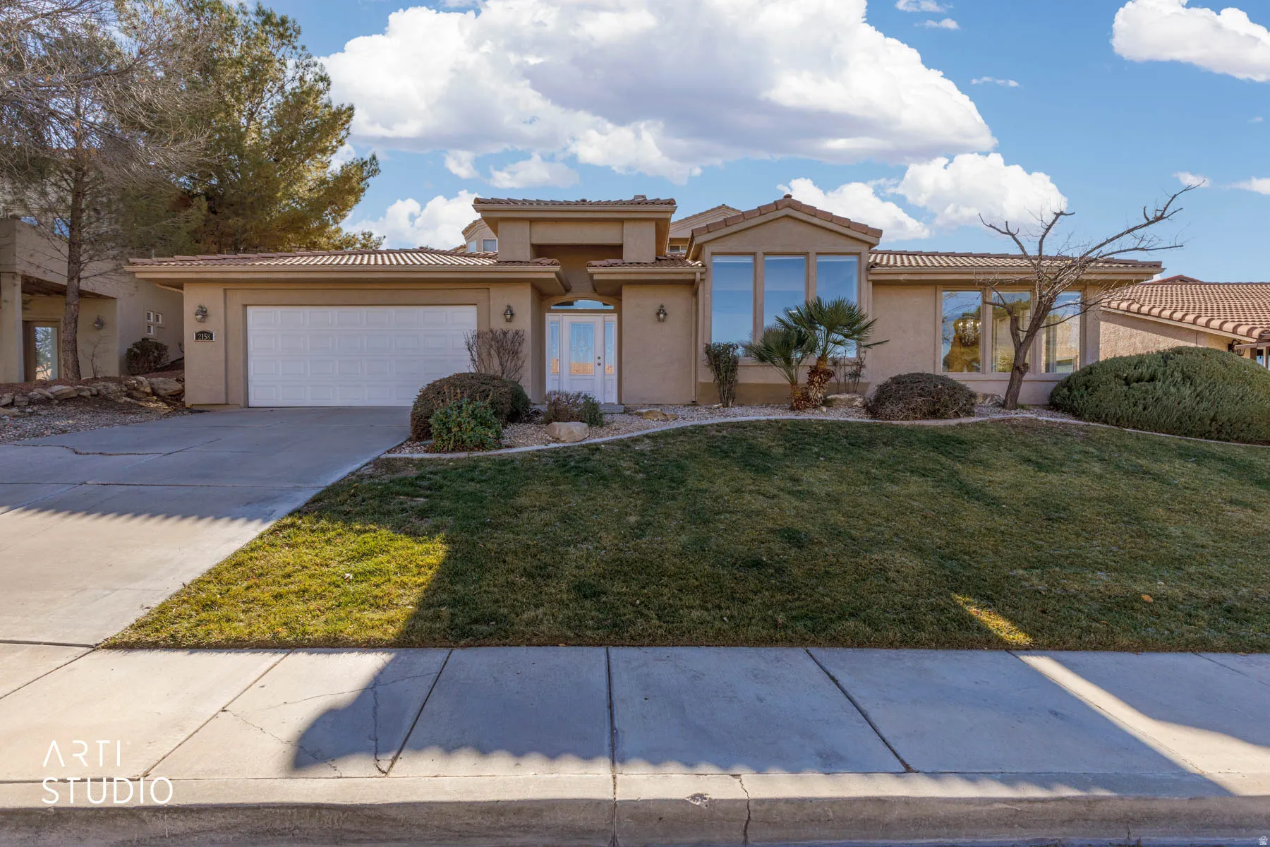 View of front facade featuring stucco siding, a tiled roof, a front lawn, driveway, and a garage