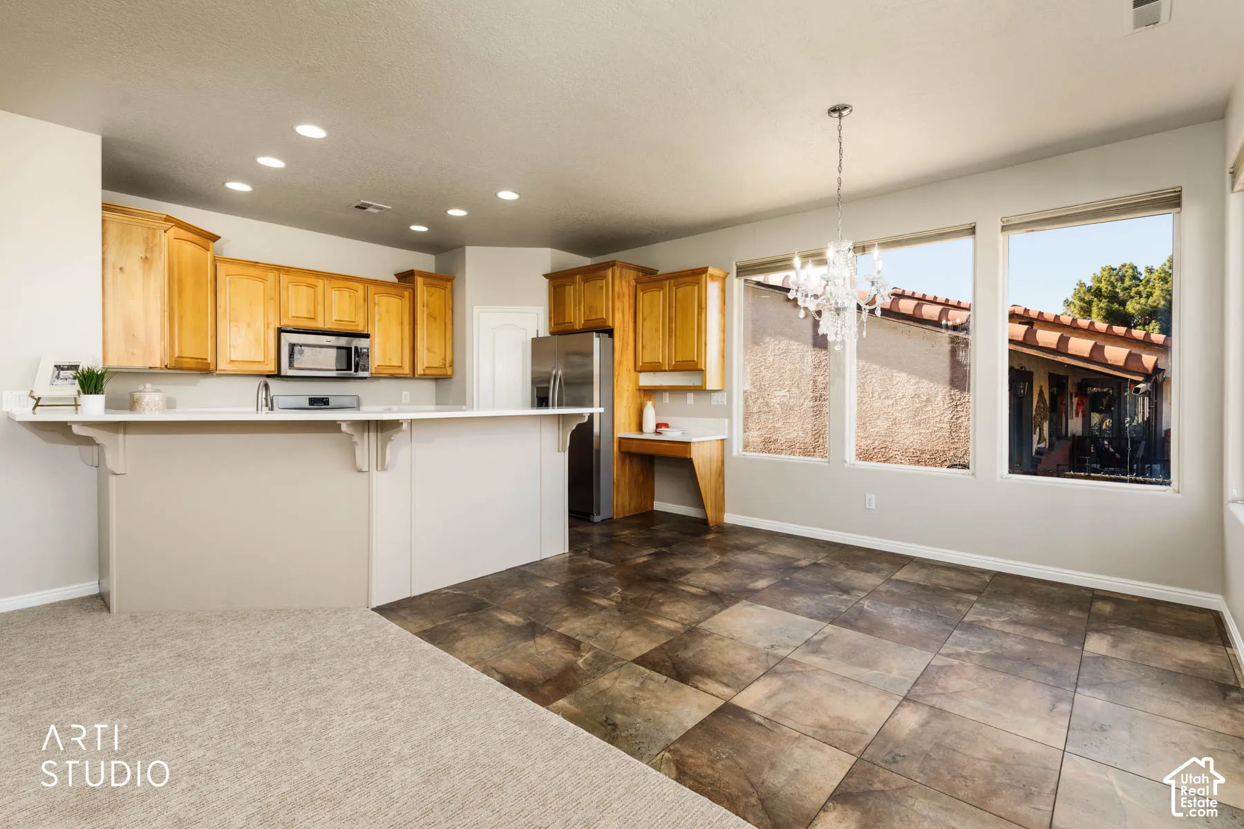 Kitchen featuring recessed lighting, a kitchen bar, a chandelier, light countertops, and appliances with stainless steel finishes