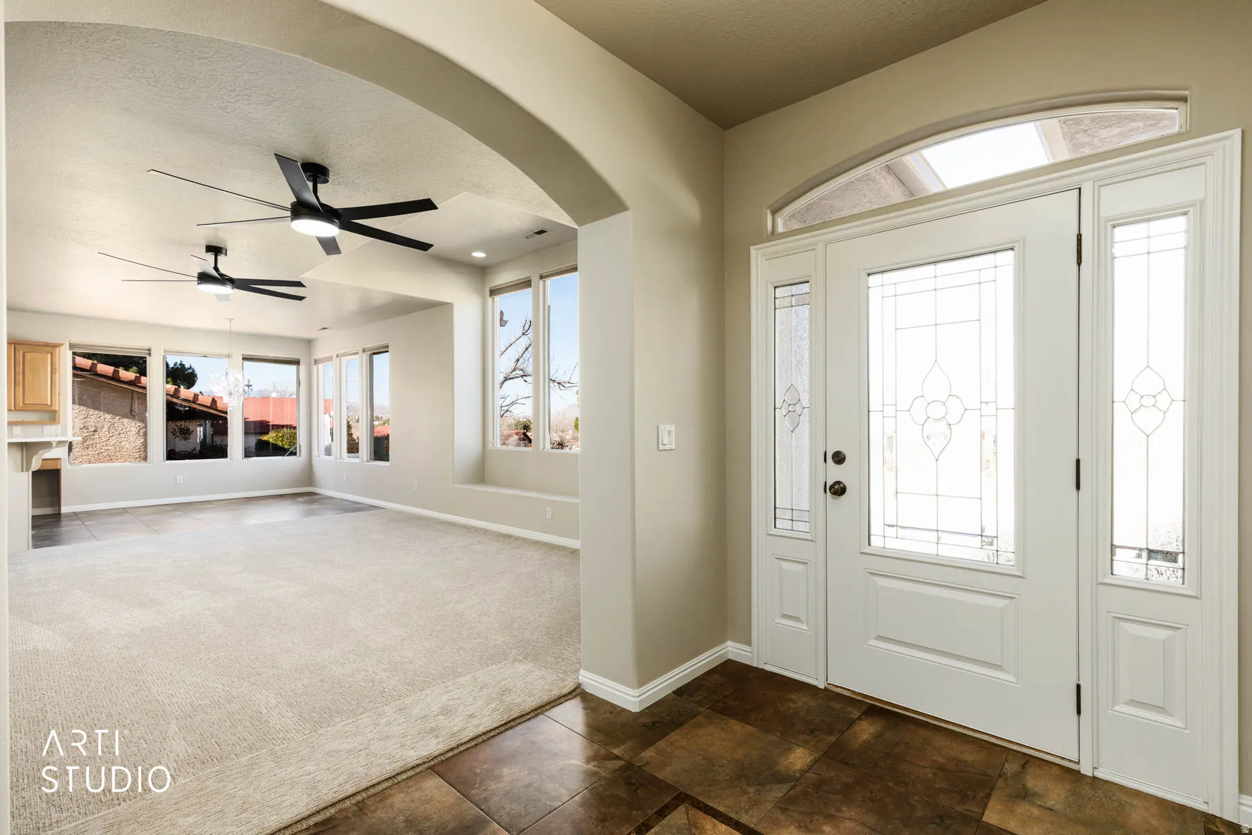Entryway with a ceiling fan, arched walkways, dark colored carpet, and a textured ceiling