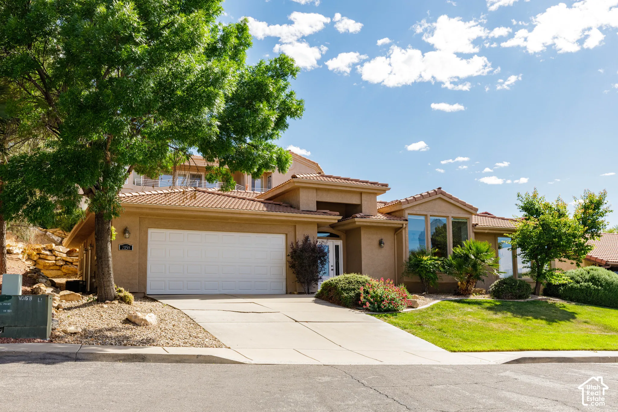 Stucco exterior home featuring a terracotta-style tile roof, a two-car garage, and multiple large windows