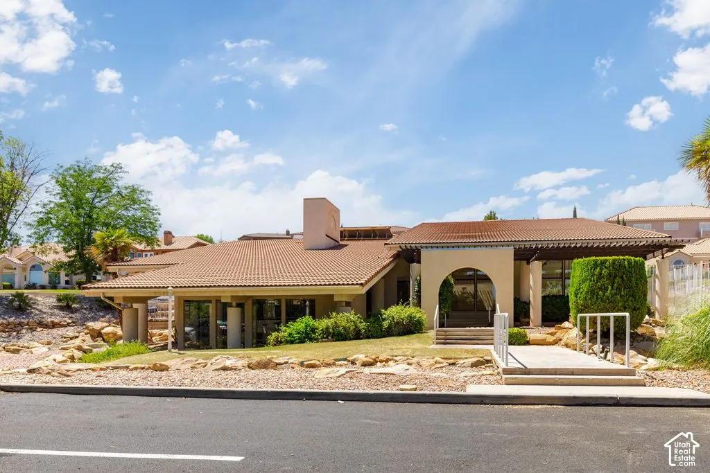 Mediterranean-style building featuring a prominent arched entry, tile roofing, and a decorative pergola