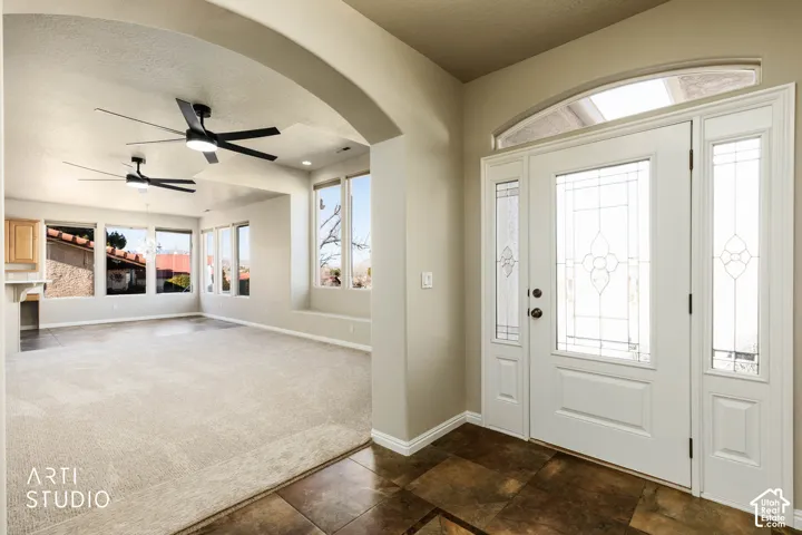 Entryway with a ceiling fan, arched walkways, dark colored carpet, and a textured ceiling