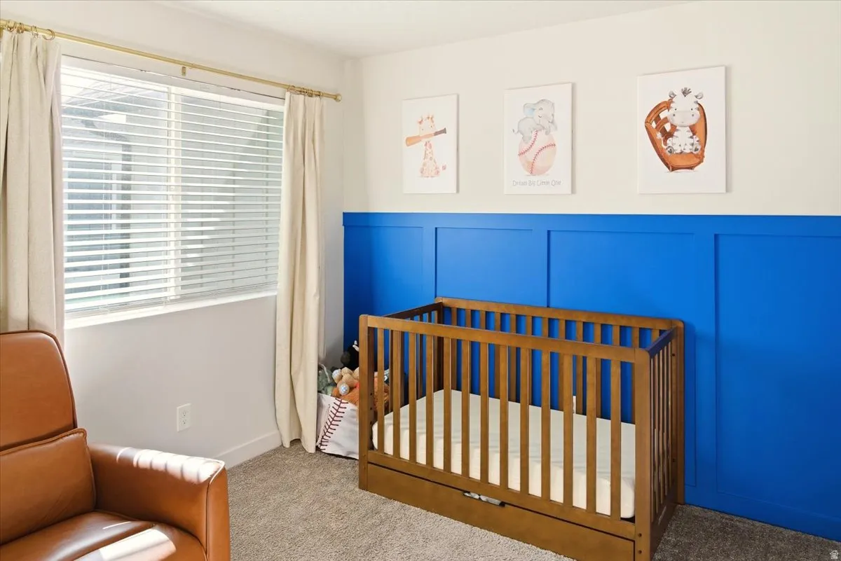 Bedroom featuring a decorative wall, a crib, carpet, and wainscoting
