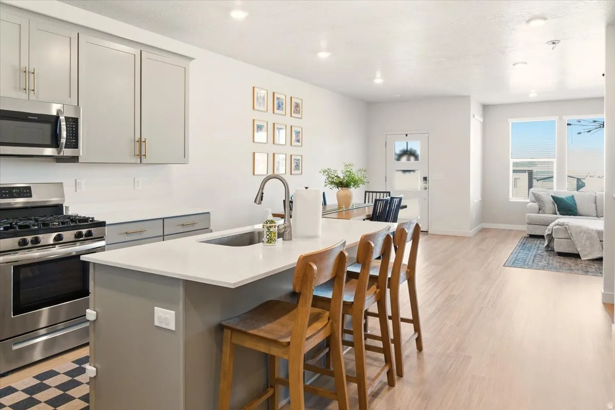 Kitchen featuring gray cabinetry, stainless steel appliances, open floor plan, a kitchen island with sink, and a breakfast bar