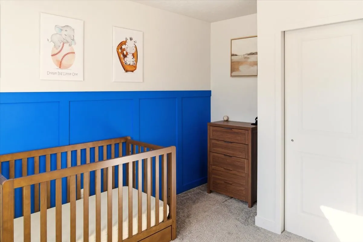 Carpeted bedroom with a decorative wall, a wainscoted wall, and a crib