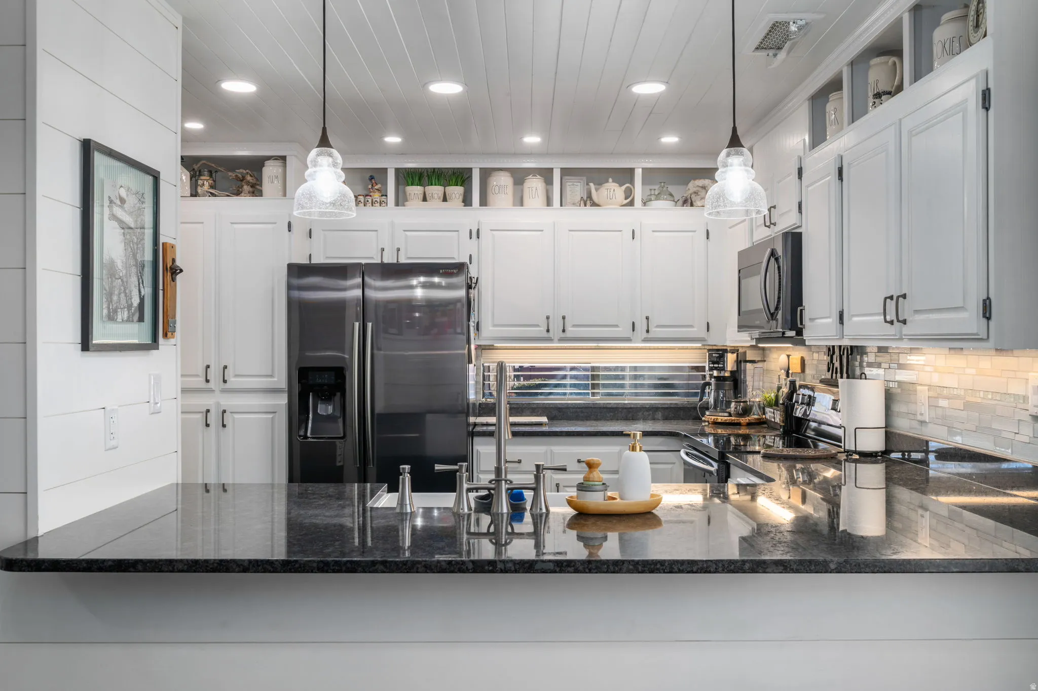Kitchen with dark stone countertops, stainless steel appliances, decorative backsplash, white cabinetry, and recessed lighting
