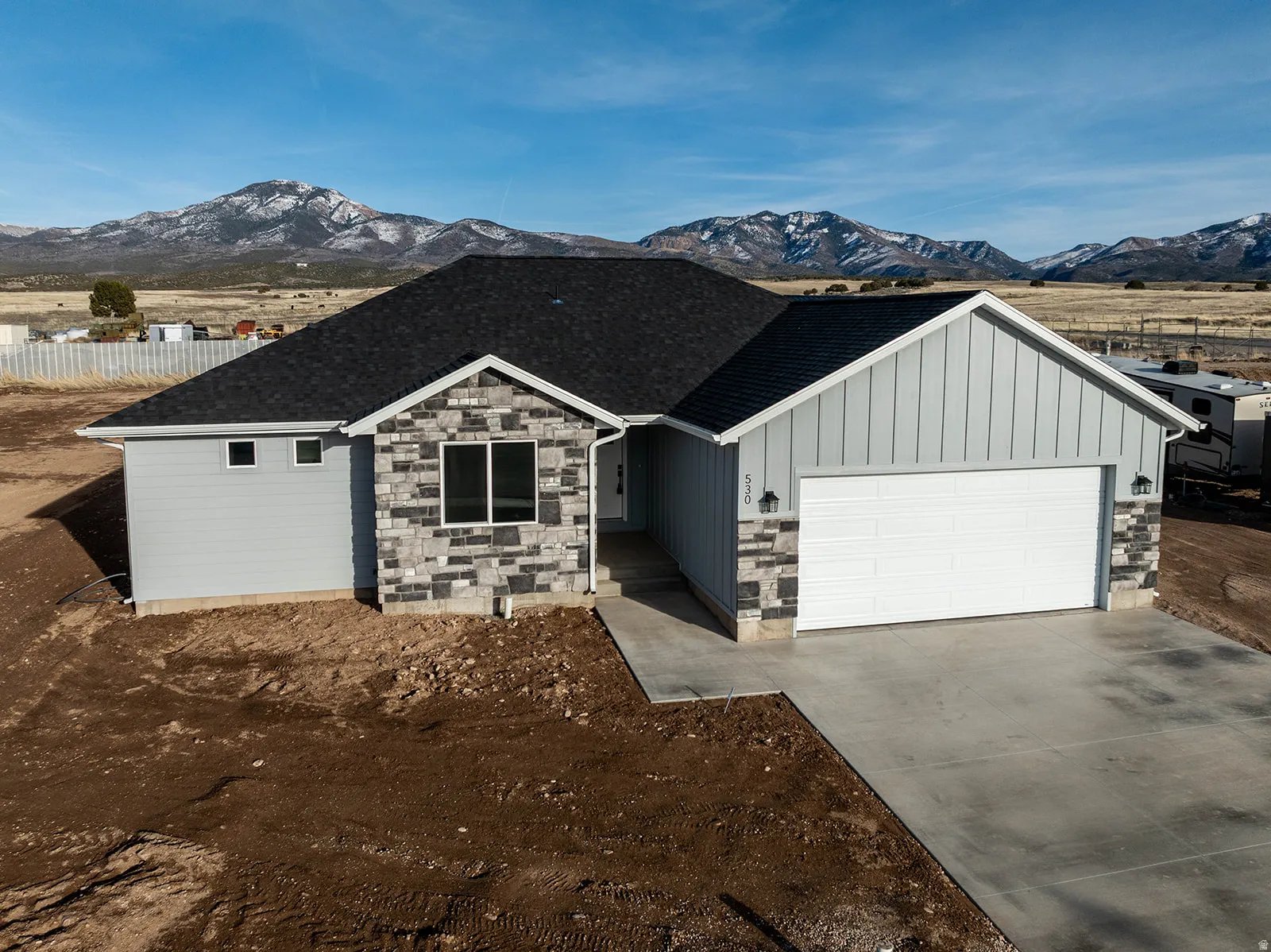Single story home featuring board and batten siding, an attached garage, concrete driveway, stone siding, and a mountain view