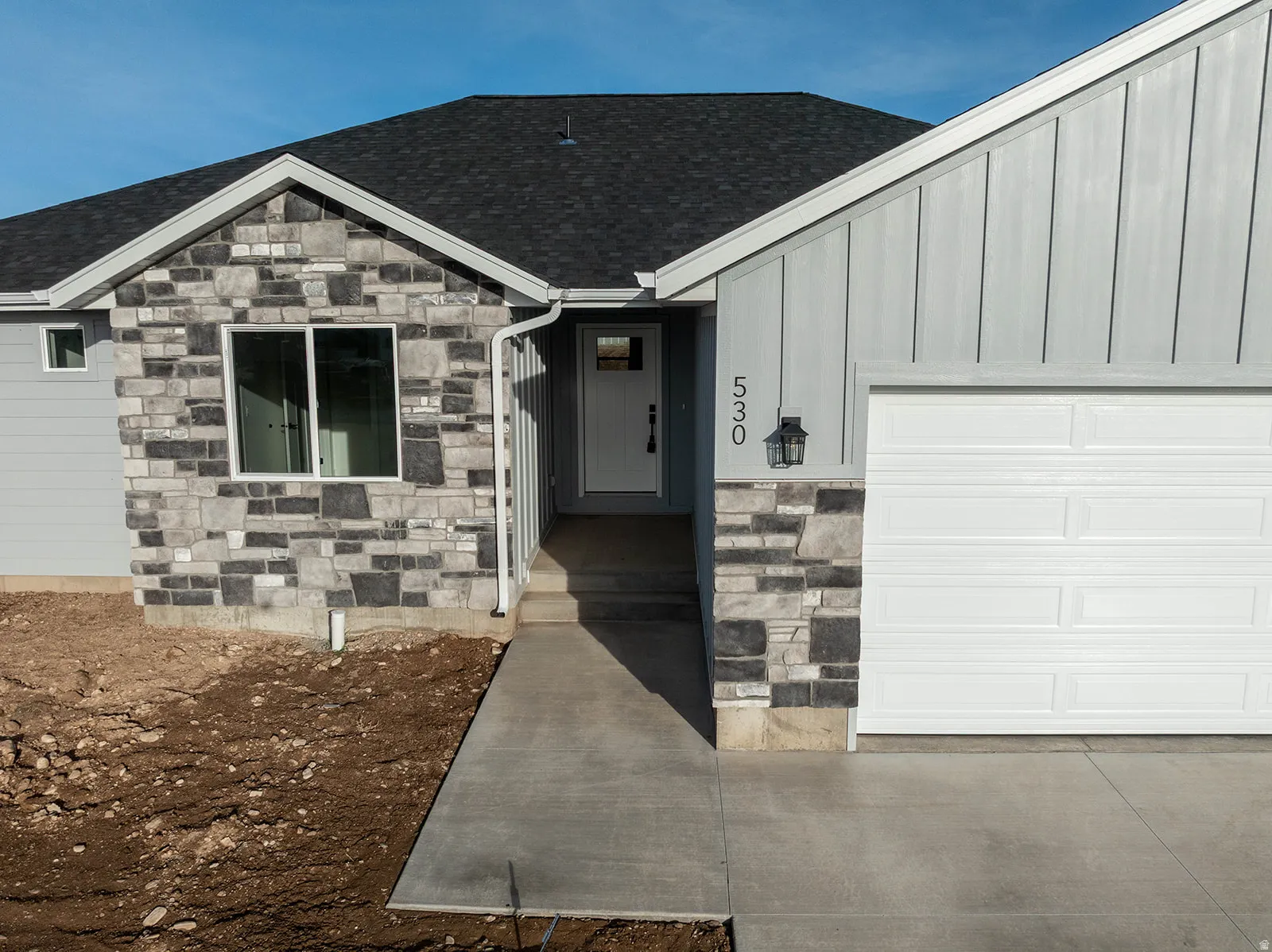 View of exterior entry with stone siding, an attached garage, board and batten siding, and roof with shingles