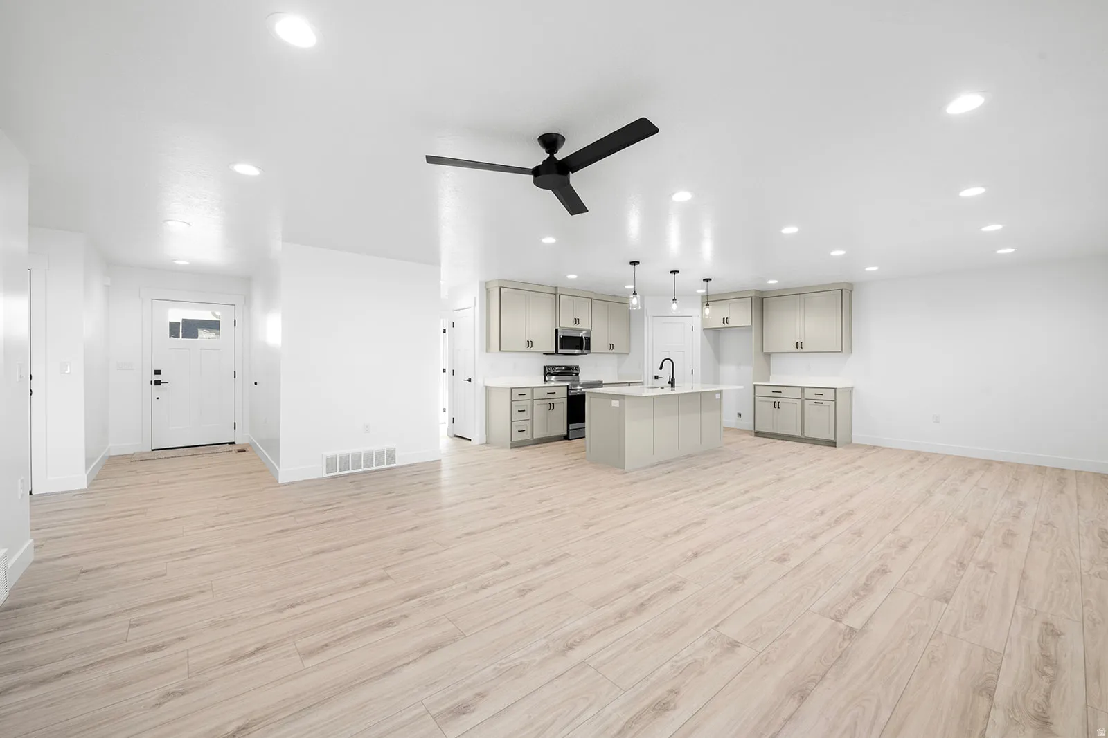 Kitchen featuring open floor plan, gray cabinetry, a ceiling fan, stainless steel appliances, and light wood-type flooring