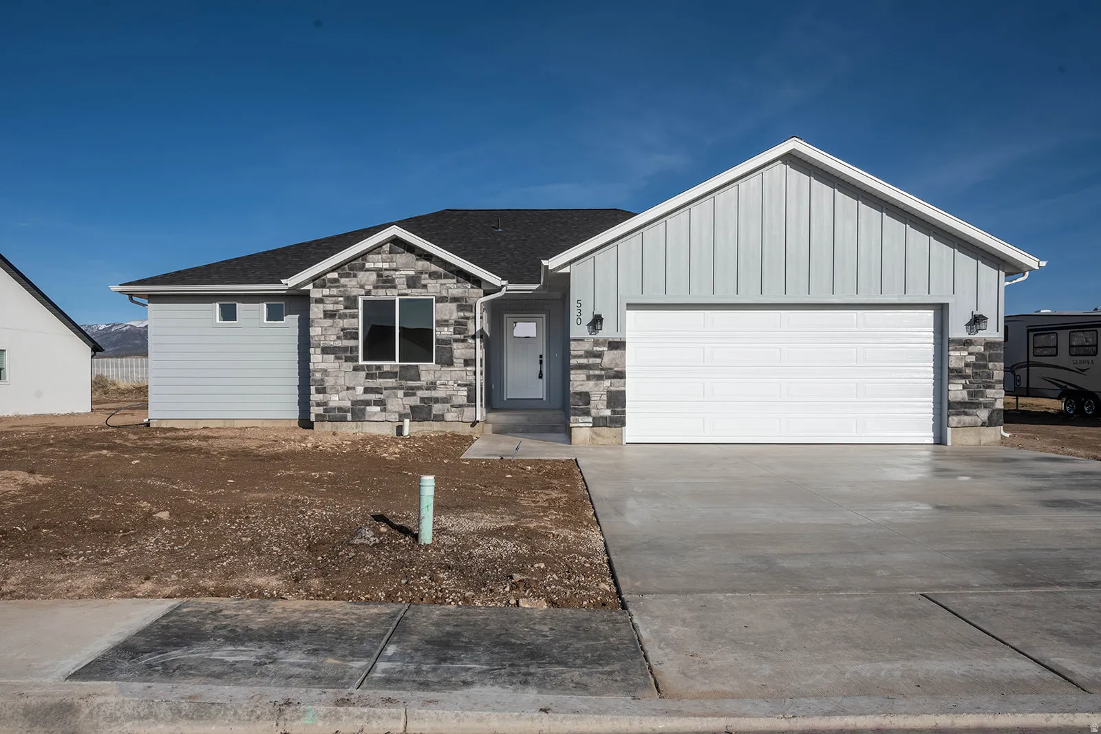 View of front facade with stone siding, driveway, a garage, and board and batten siding