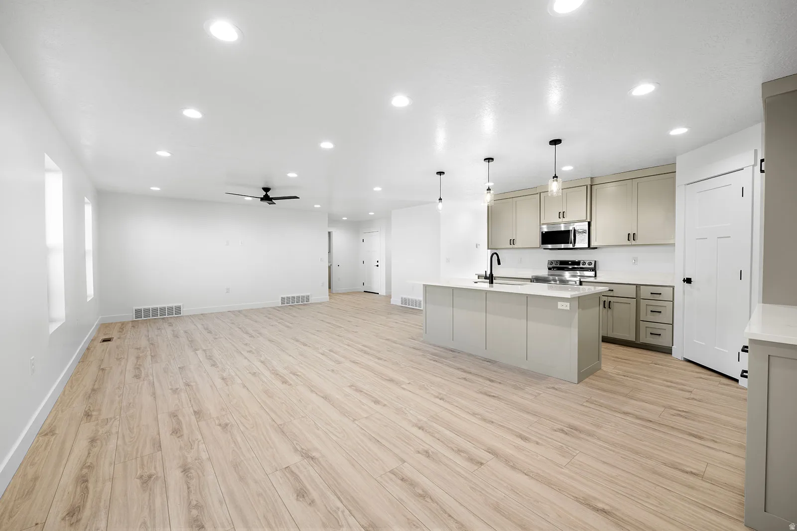 Kitchen with open floor plan, stainless steel appliances, pendant lighting, a kitchen island with sink, and light wood-style flooring