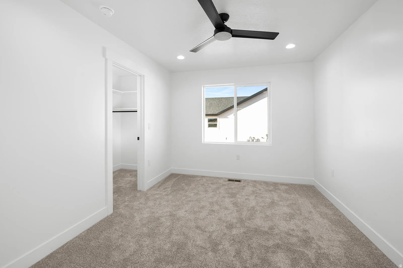 Unfurnished bedroom featuring a spacious closet, light colored carpet, and a ceiling fan