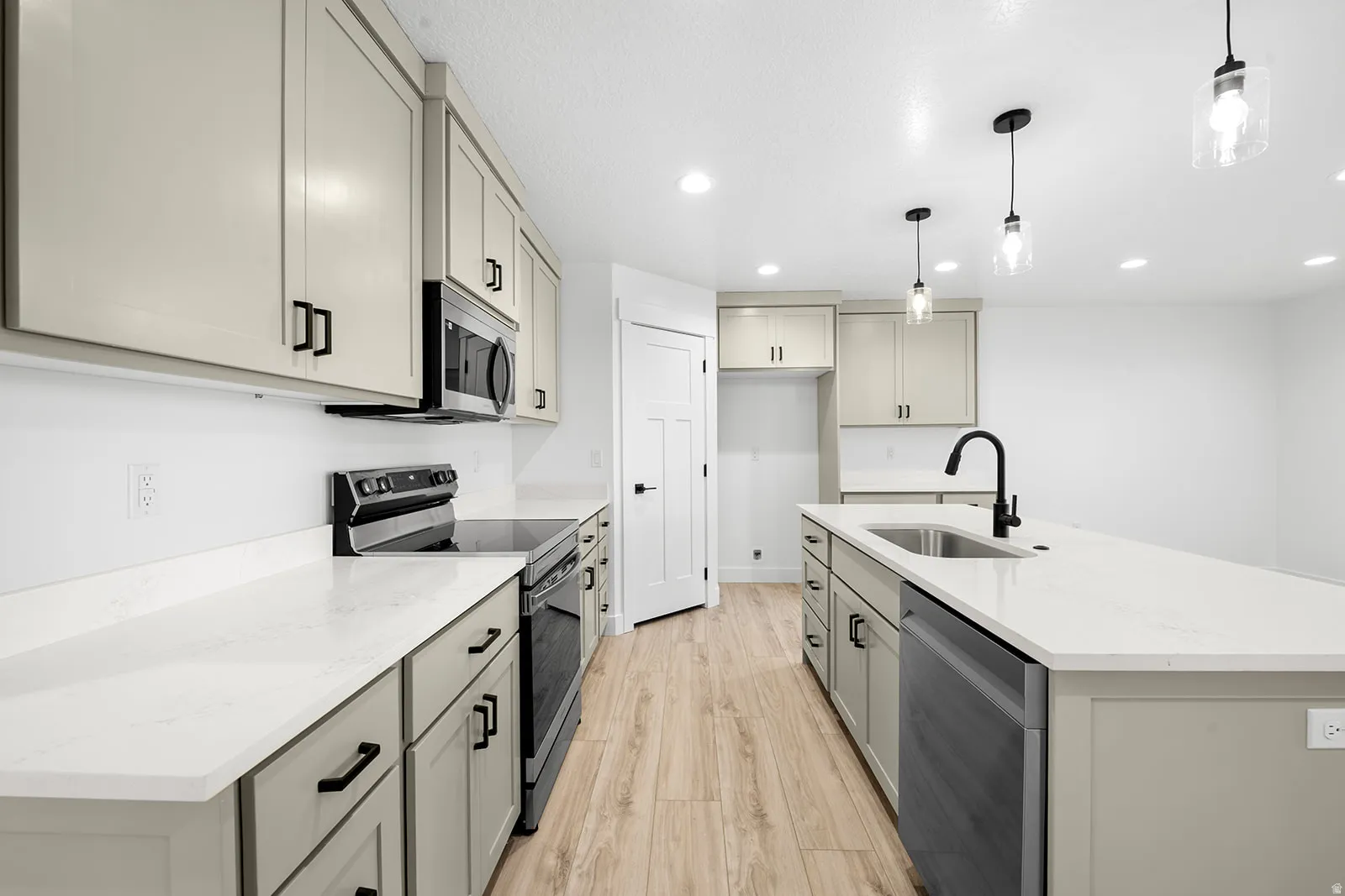 Kitchen with stainless steel appliances, gray cabinets, a center island with sink, light wood-type flooring, and light stone countertops