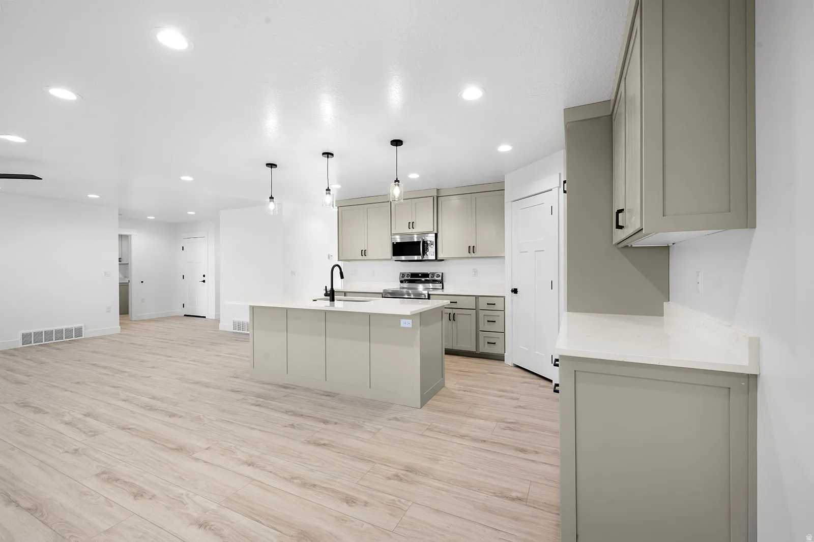 Kitchen featuring gray cabinetry, light wood-style floors, stainless steel appliances, light stone countertops, and a center island with sink