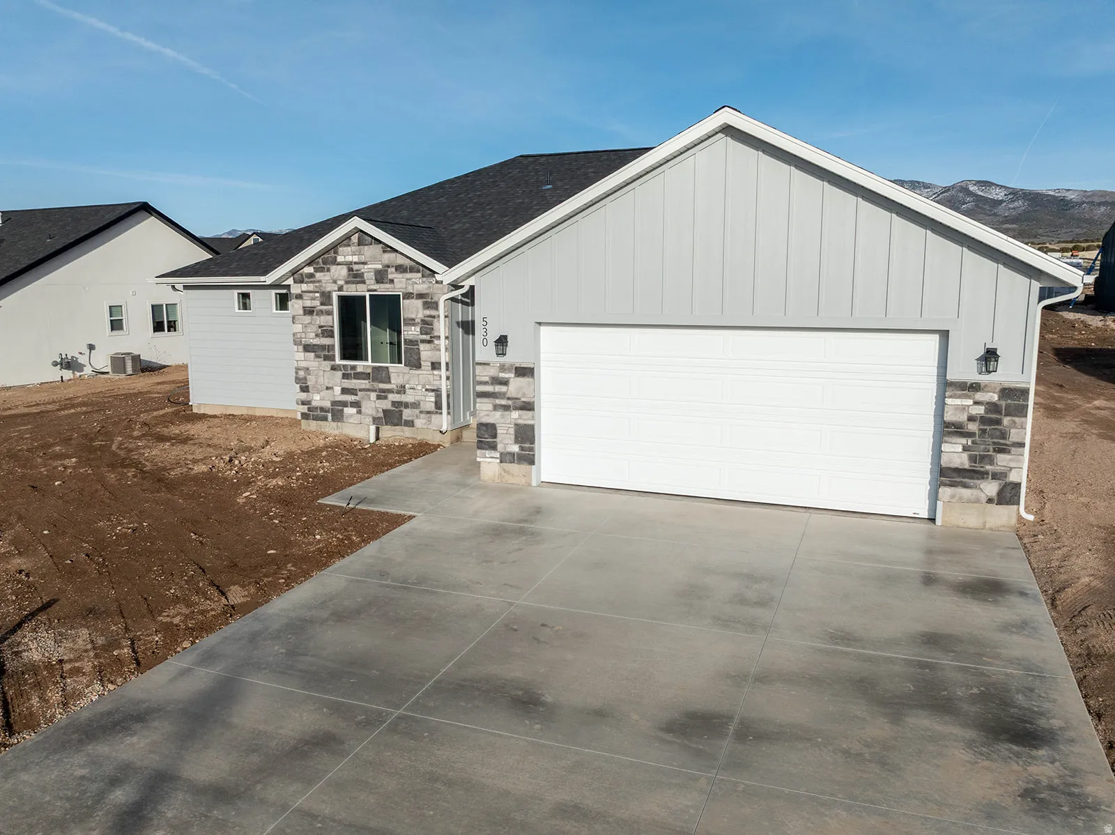 Ranch-style house featuring stone siding, an attached garage, concrete driveway, and board and batten siding