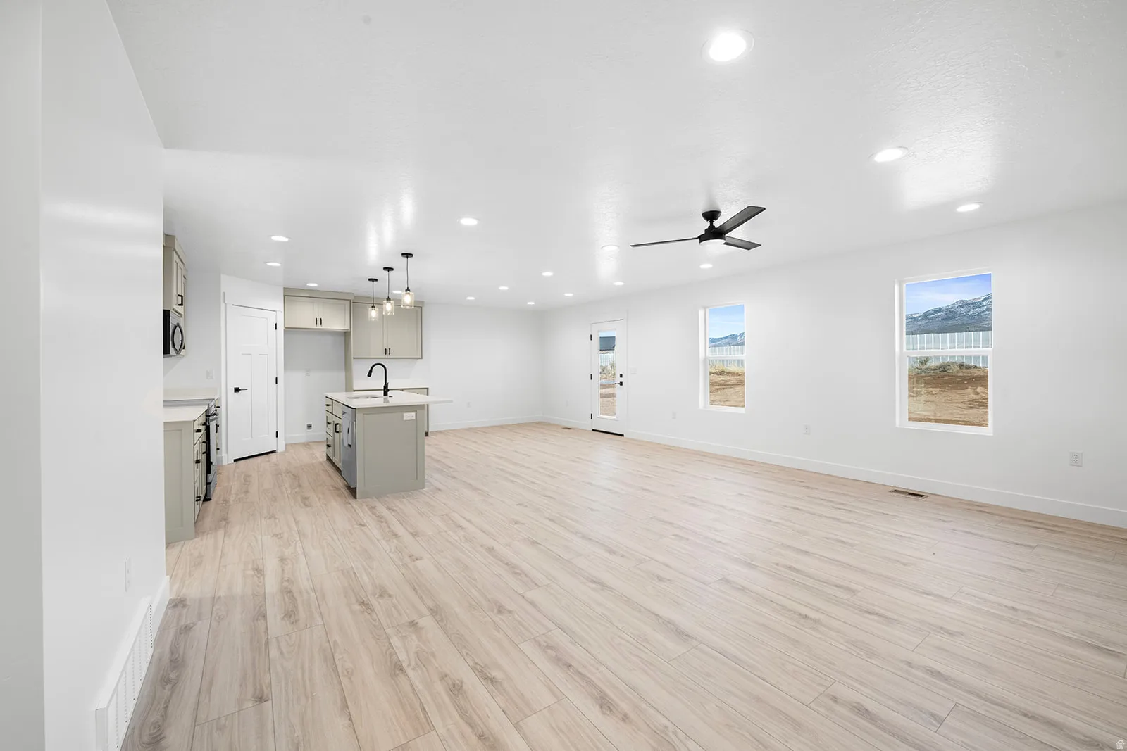 Kitchen featuring open floor plan, gray cabinetry, a kitchen island with sink, light wood-type flooring, and decorative light fixtures