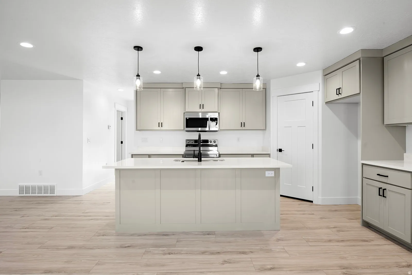 Kitchen featuring gray cabinetry, light wood-style flooring, stainless steel appliances, and light stone counters