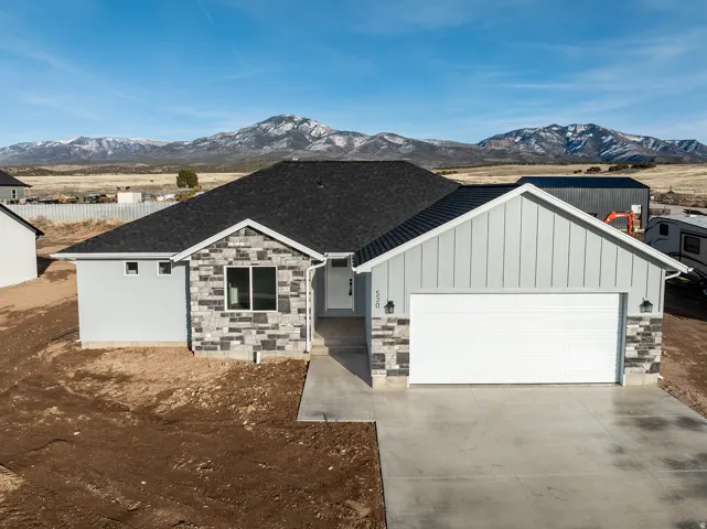 View of front of home with an attached garage, stone siding, driveway, and board and batten siding