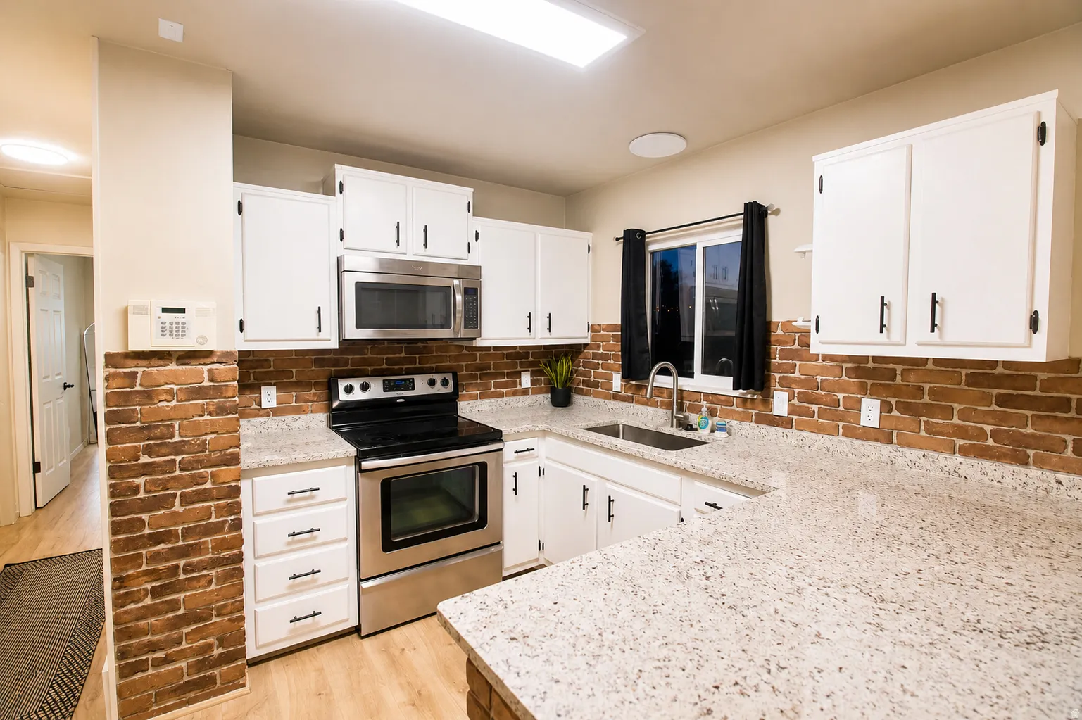 Kitchen featuring stainless steel appliances, light stone counters, white cabinets, and light wood-type flooring