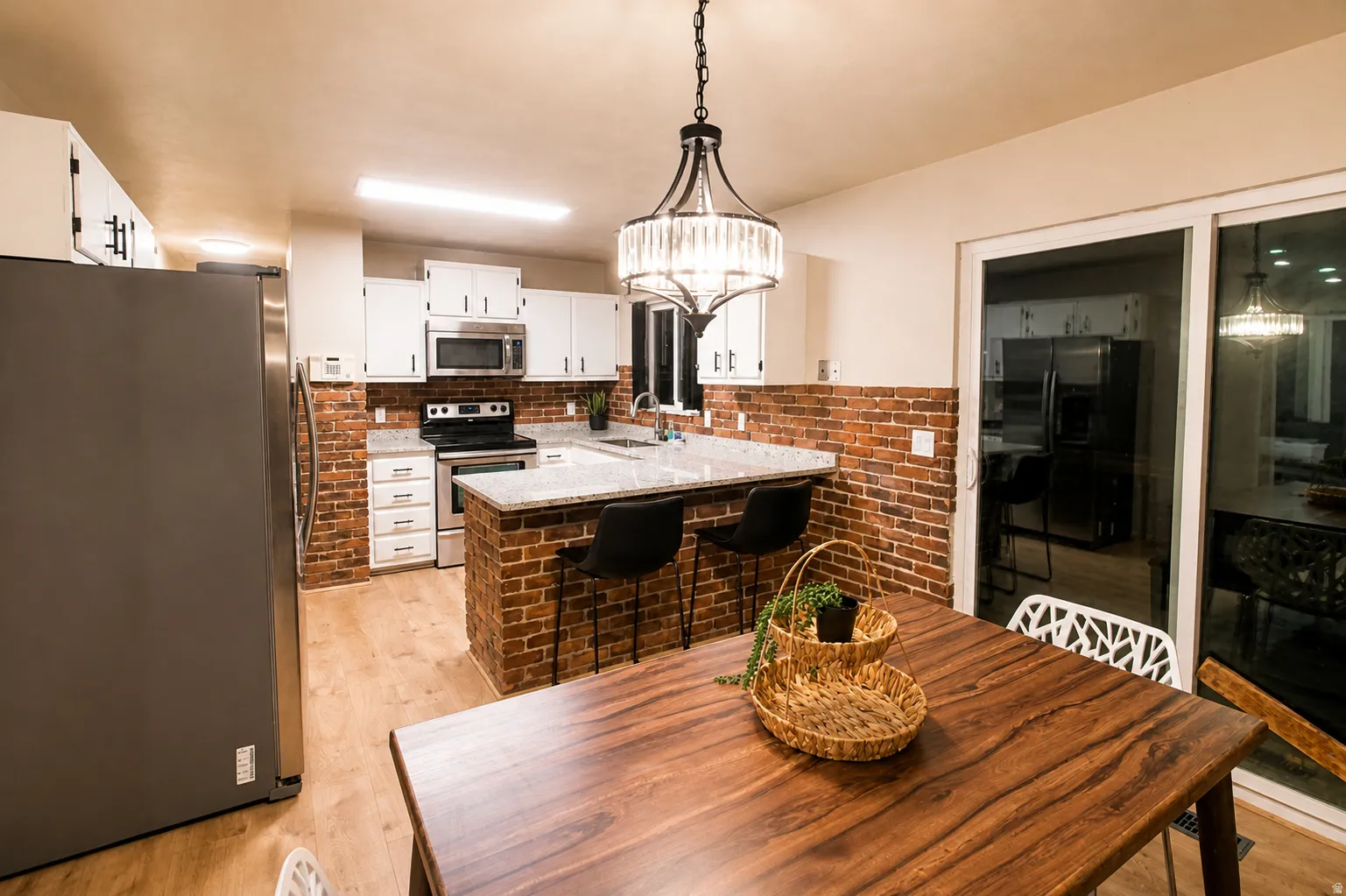 Kitchen featuring stainless steel appliances, white cabinets, light wood-style flooring, a peninsula, and a kitchen bar