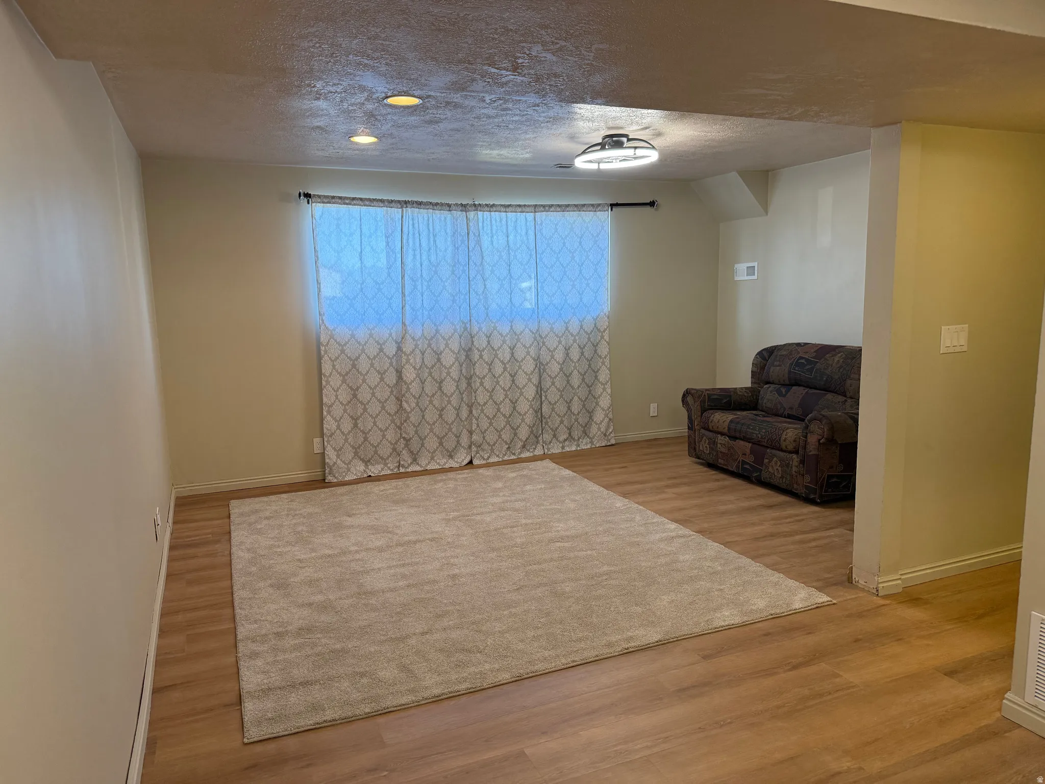 Room featuring wood-finish flooring, recessed lighting, a window with patterned curtains, and a ceiling-mounted light fixture