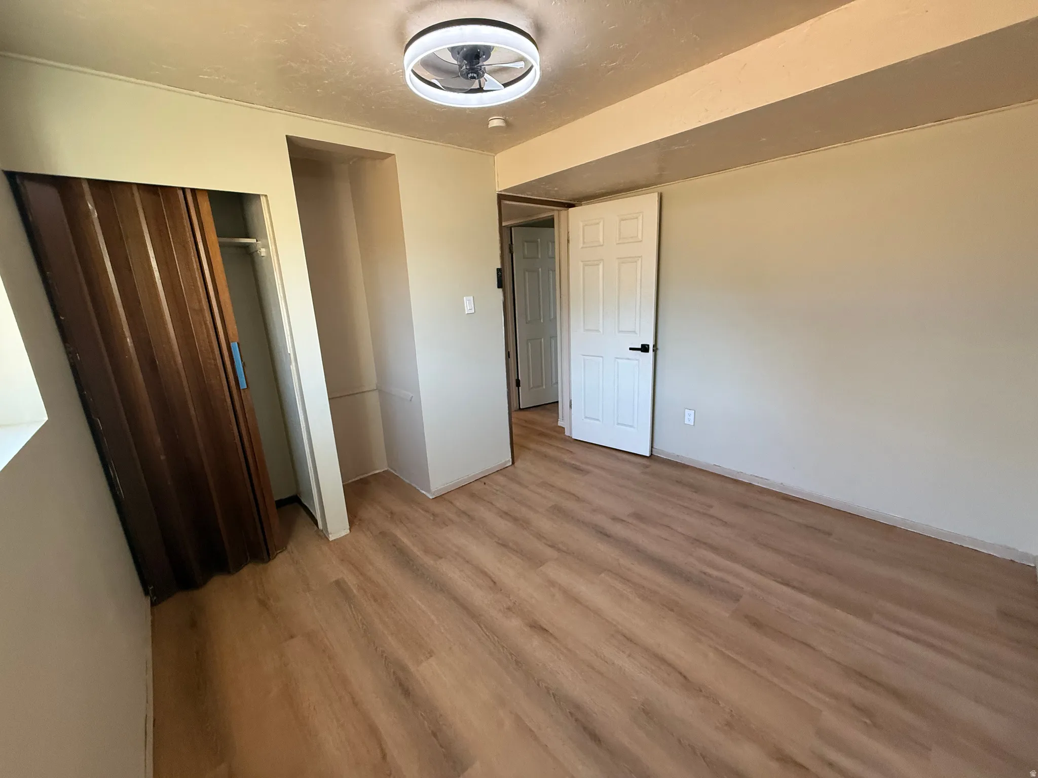 Neutral-toned room featuring wood-finish flooring, a contemporary ceiling light fixture with integrated fan, and light-colored walls