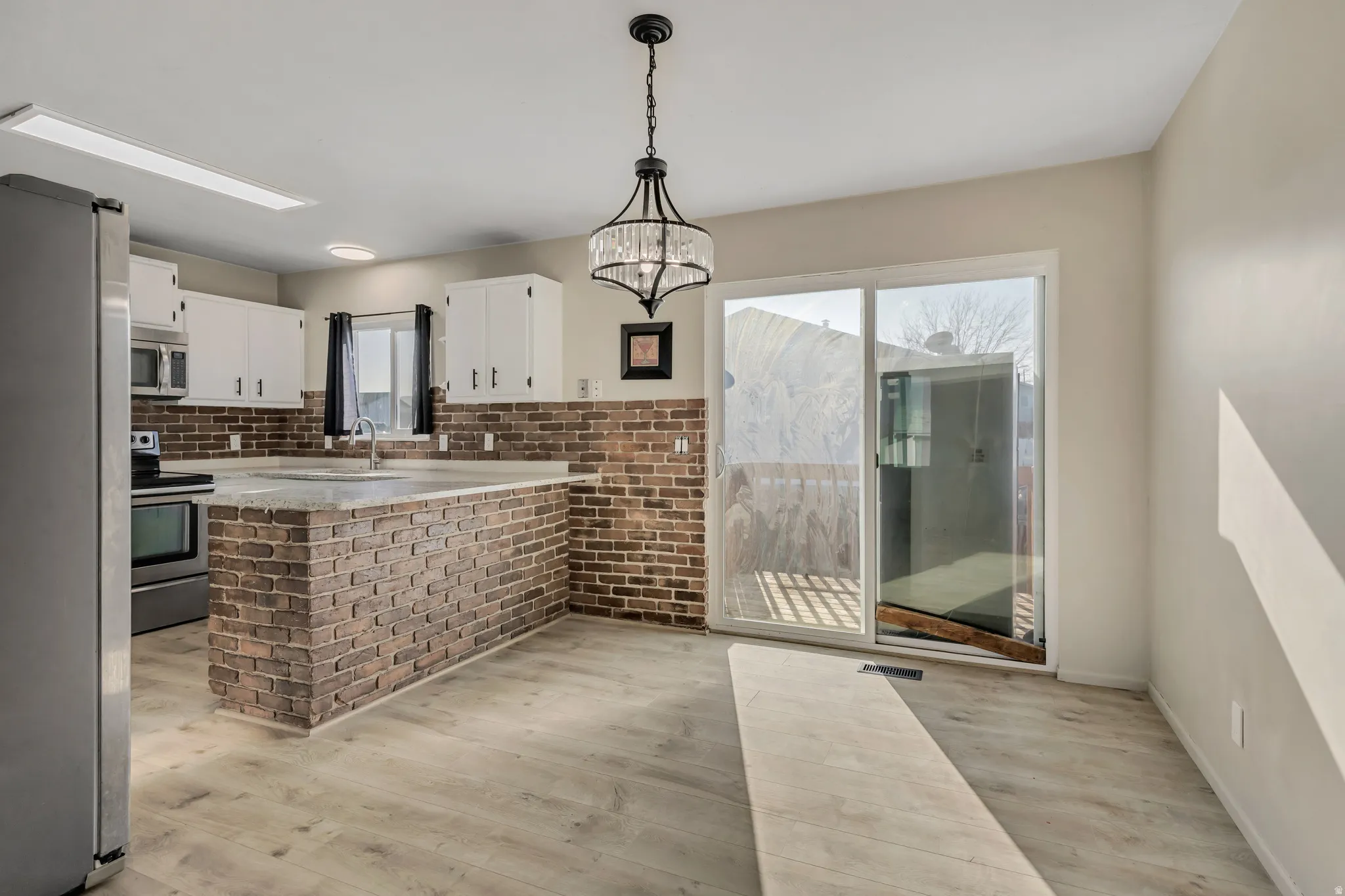 Kitchen with a peninsula, stainless steel appliances, hanging light fixtures, white cabinets, and light wood laminate flooring