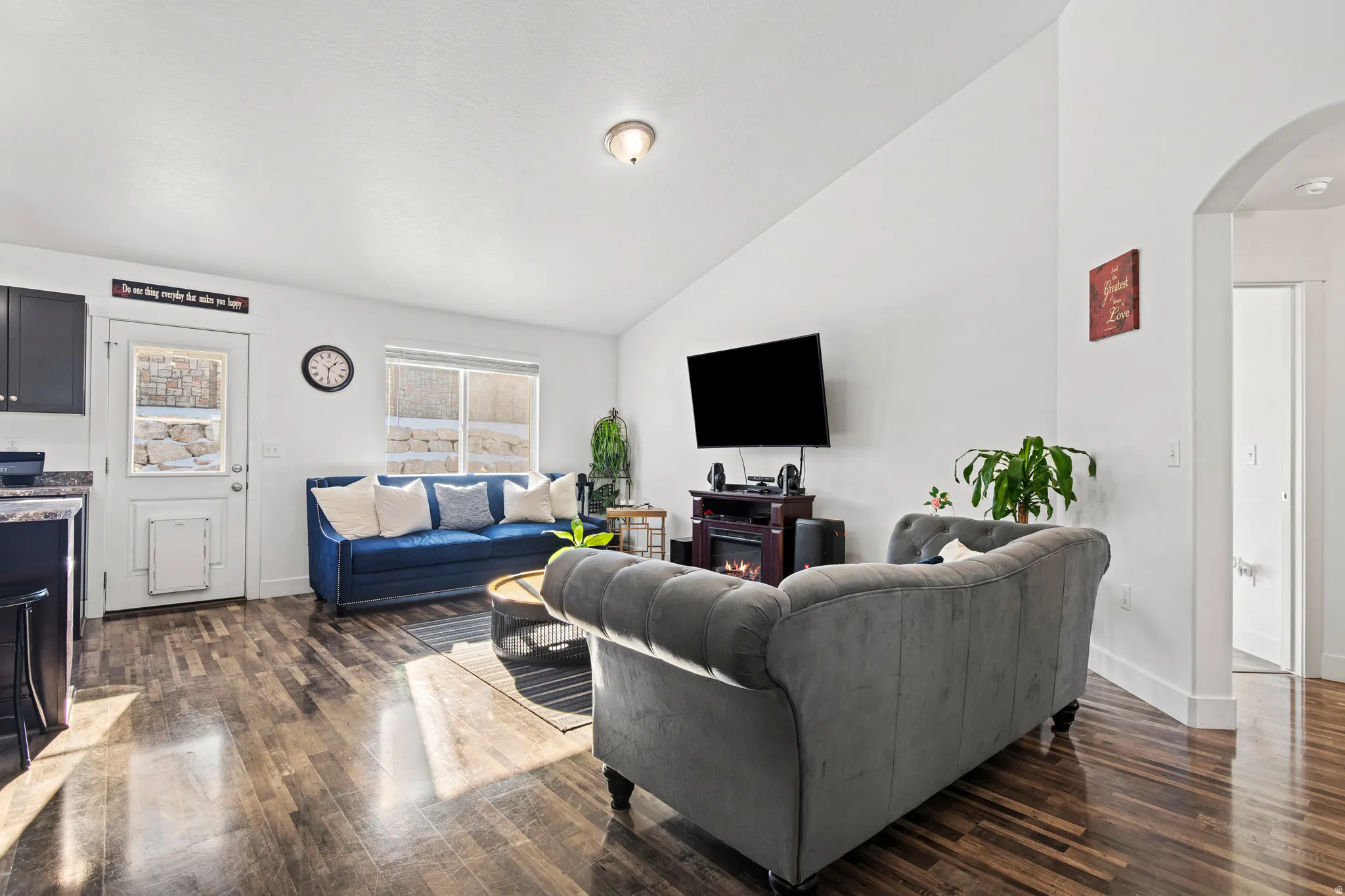 Living room with a warm lit fireplace, vaulted ceiling, arched walkways, and dark wood-style floors