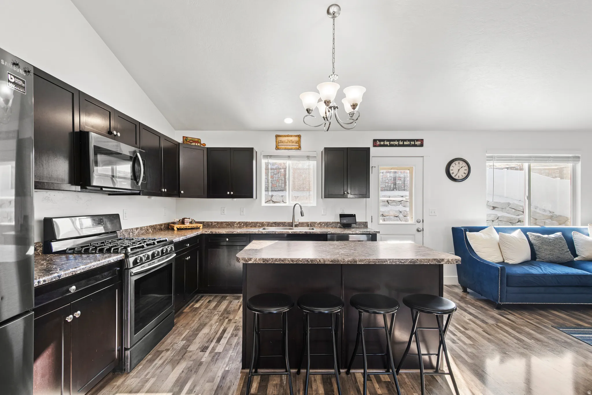 Kitchen with appliances with stainless steel finishes, a kitchen island, hanging light fixtures, a kitchen bar, and vaulted ceiling