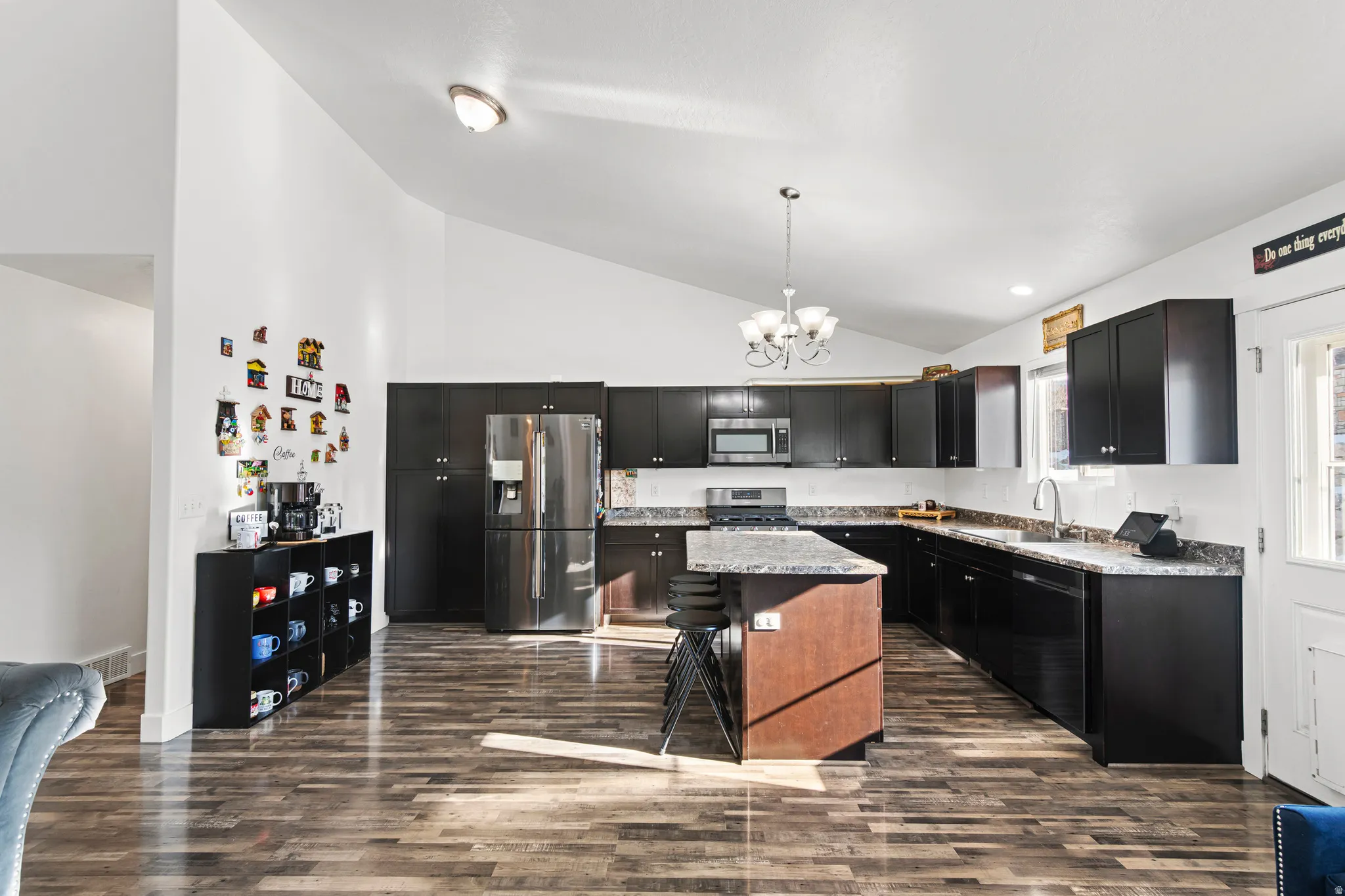 Kitchen with dark cabinets, stainless steel appliances, a kitchen island, a kitchen breakfast bar, and hanging light fixtures