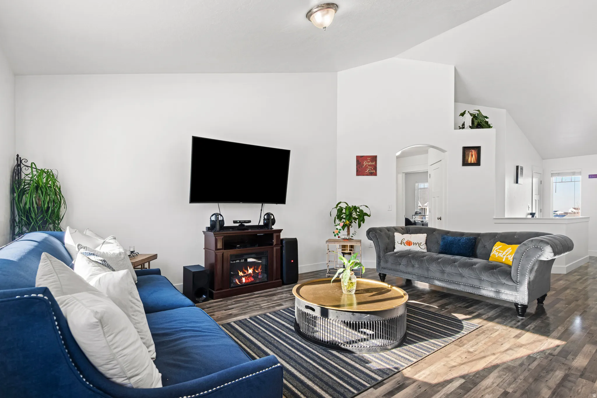 Living room with arched walkways, wood finished floors, lofted ceiling, and a glass covered fireplace